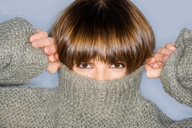 Close-up of a young woman, covering her face in turtleneck --- Image by © Glowimages/Corbis